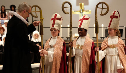 Hauptpastor und Propst Martin Vetter legt Christian Kratzsch (11), Raphael Owuso Opuko (10) und Mila Jandt (10) das Bischofskreuz um (von links) - Copyright: Rauhes Haus / Stephan Wallocha