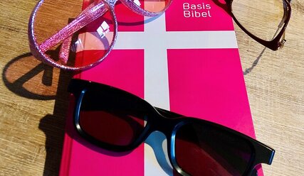 Rotes Buch mit Kreuz auf dem Deckel, Titel Basis-Bibel, darauf zwei Brillen, 1 Sonnenbrille - Copyright: Saskia Albers