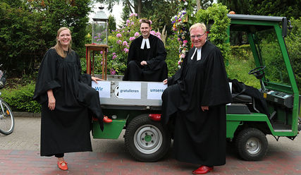 Pastorin Laura Koch-Pauka, Vikar Alexander Bieniasz und Pastor Harald Schmidt sitzen auf einem kleinen Trekker, dem Konfi-Mobil. - Copyright: Sandra Bähr