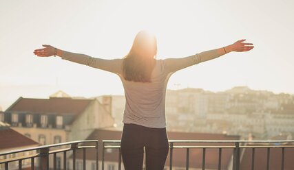 Frau auf dem Balkon mit ausgebreiteten Armen mit Blick auf eine Stadt - Copyright: Pexels