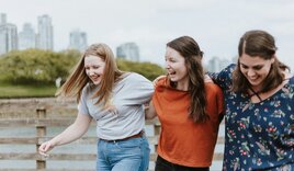 Drei junge Frauen am Wasser vor der Skyline einer Großstadt. - Copyright: Unsplash