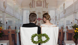 Ein angehendes Hochzeitspaar nimmt auf den Stühlen vor der Bannerwand Platz, die den Altarraum abbildet.  - Copyright: Thomas Krätzig