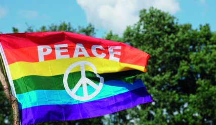 Rot-gelb-grün-hellblau-blau gestreifte wehendeFlagge mit Aufschrift PEACE und Friedenssymbol. - Copyright: Ben_Frieden, Pixabay