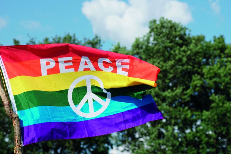 Rot-gelb-grün-hellblau-blau gestreifte wehendeFlagge mit Aufschrift PEACE und Friedenssymbol.
