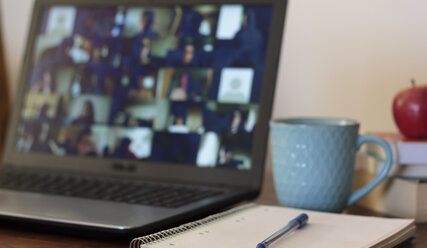 Das Bild zeigt einen Tisch auf dem ein eingeschaltetes Notebook, ein Schreibblock mit Stift, ein Kaffeebecher, drei gestapelte Bücher und ein Apfel liegen. - Copyright: iStockPhoto