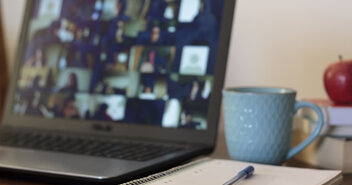 Das Bild zeigt einen Tisch auf dem ein eingeschaltetes Notebook, ein Schreibblock mit Stift, ein Kaffeebecher, drei gestapelte Bücher und ein Apfel liegen. - Copyright: iStockPhoto