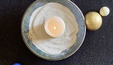 Eine brennende Kerze in einer mit Sand gefüllten Schale und ein Kreuz und Perlen darum herum - Copyright: Wiebke Meers